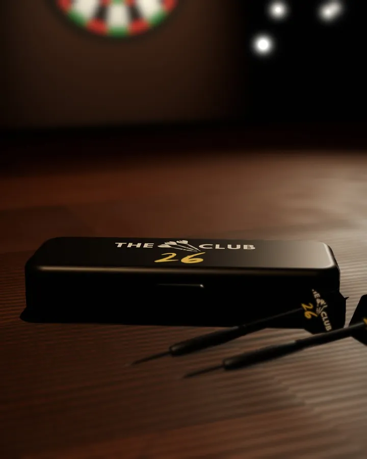 Render of the black hinged dart case, closed, with The 26 Club logo in white and gold on the lid, on a pub table beside two darts