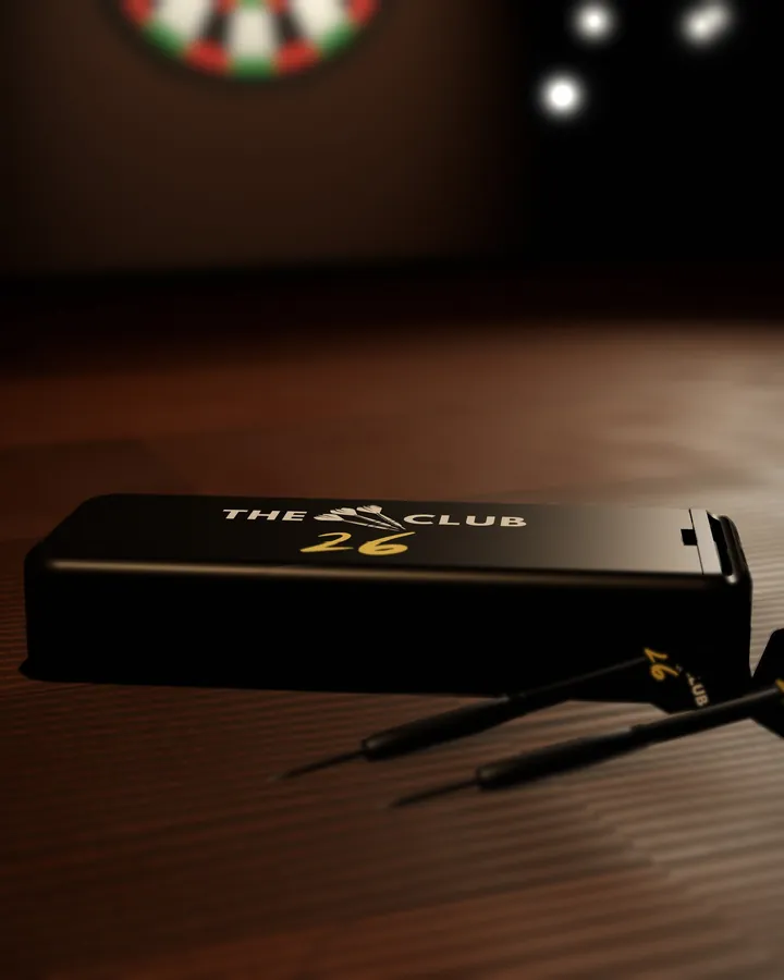 Render of the black drawer dart case, closed, with The 26 Club logo in white and gold on top, on a pub table beside two darts